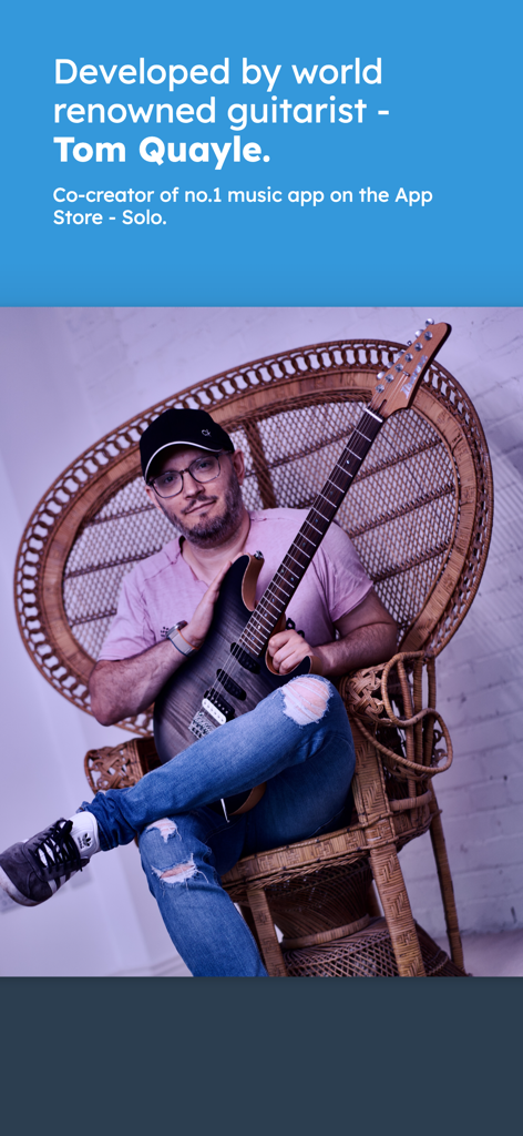 Metric Flow - Guitarrista de renombre mundial Tom Quayle sosteniendo una guitarra eléctrica en una silla de mimbre