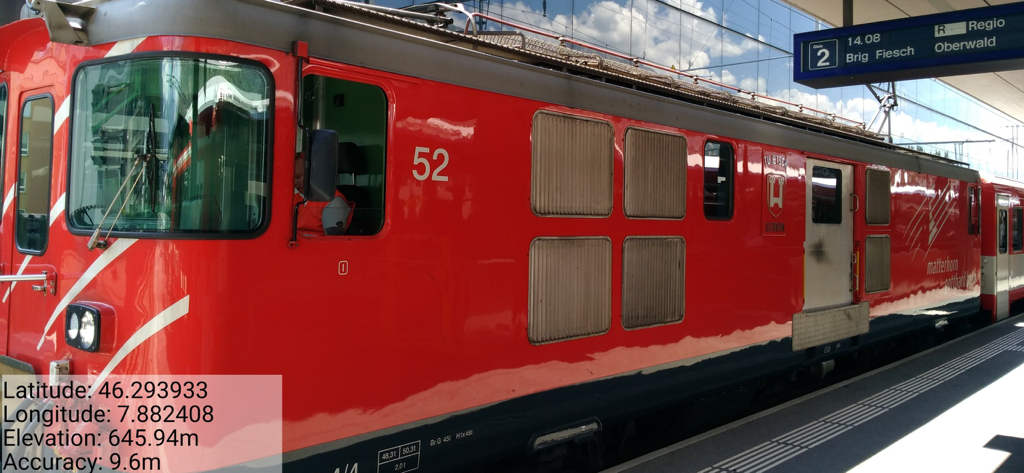 NoteCam - photo with notes - 駅の赤い列車の写真に、GPS座標と高度を示すNoteCamのデータオーバーレイが表示されています。