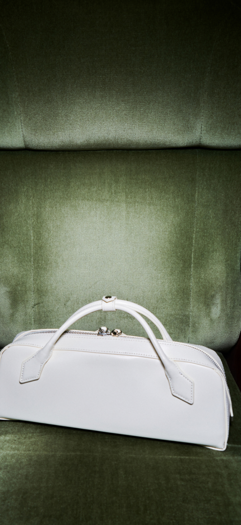 Rendez-Vous – магазин - Elegant white leather luxury handbag sitting on a plush green velvet chair.