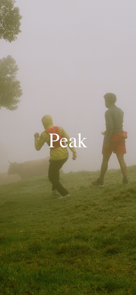 Peak store - Two people wearing technical outdoor clothing in a misty green field with the word Peak displayed in the center.