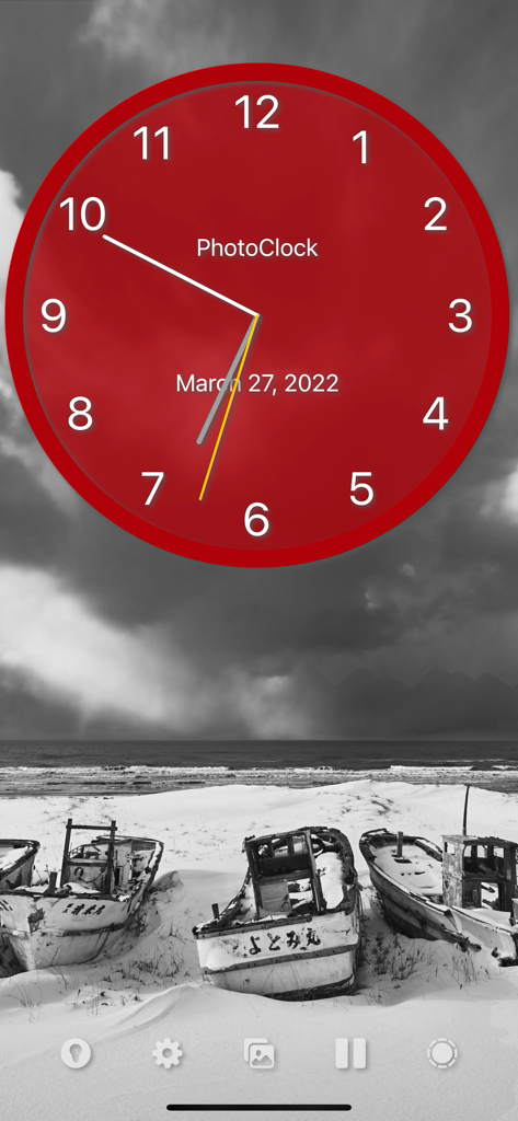 PhotoClock Pro - A red analog clock face over a black and white photo of abandoned boats on a beach