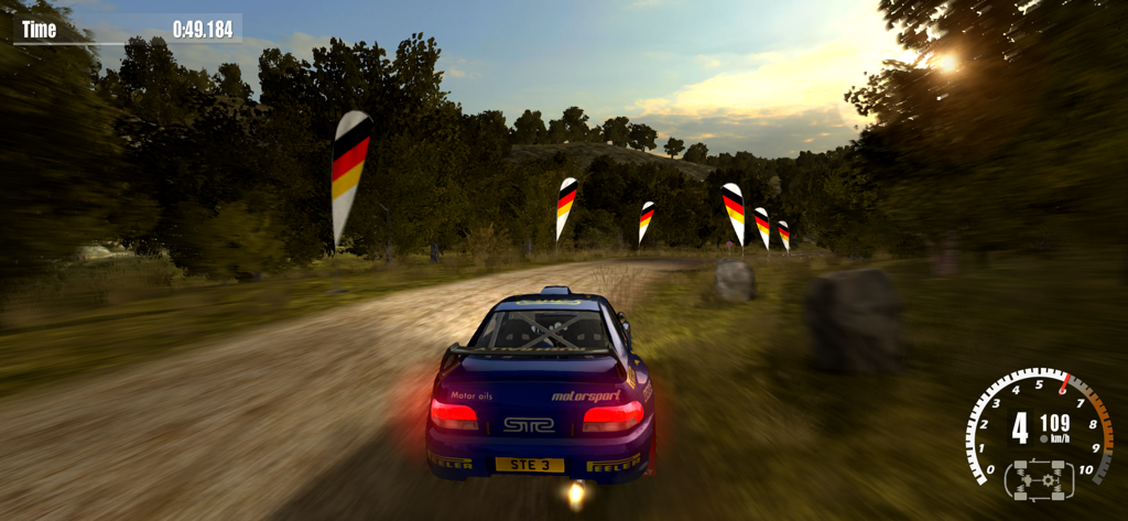 Rush Rally 3 - A blue rally car racing on a dirt track through a forest at sunset.