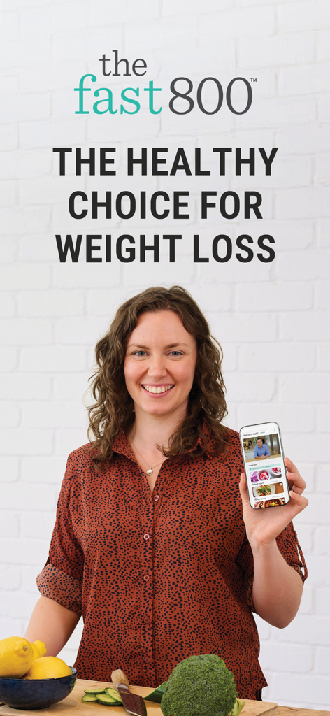 A smiling woman holding a smartphone displaying The Fast 800 app interface next to fresh broccoli and lemons
