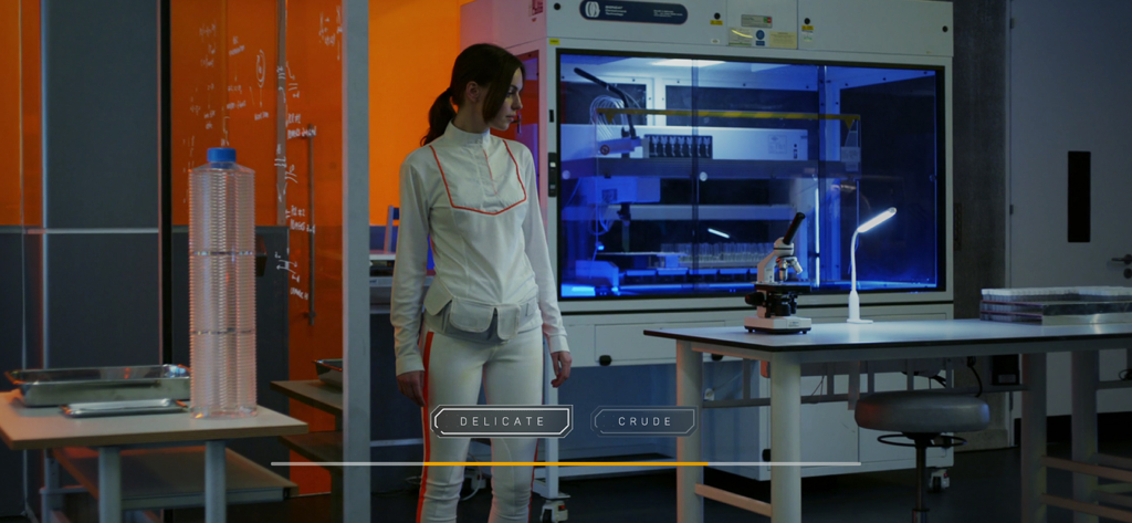 Una mujer con uniforme blanco de pie en un laboratorio de alta tecnología con botones interactivos de juego para elegir entre Delicada y Cruda
