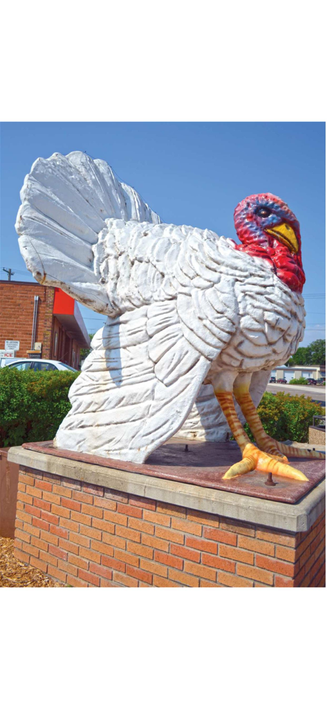 American Road Magazine - A large white turkey statue with a red and blue head sitting on a brick pedestal, representing a classic American roadside attraction.