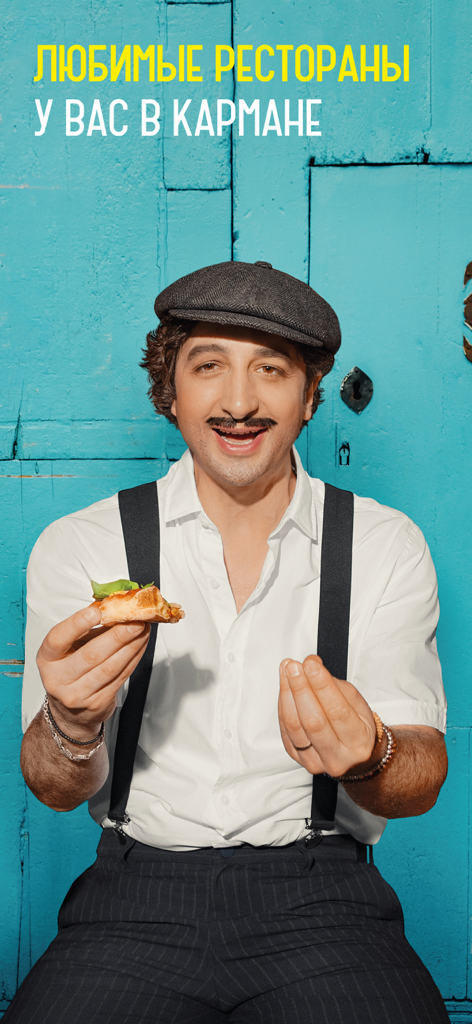 Un hombre con tirantes sosteniendo una porción de pizza contra un fondo azul brillante