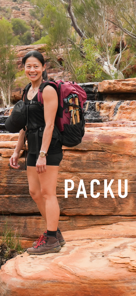 A smiling woman with a large red backpack standing on red rock layers.