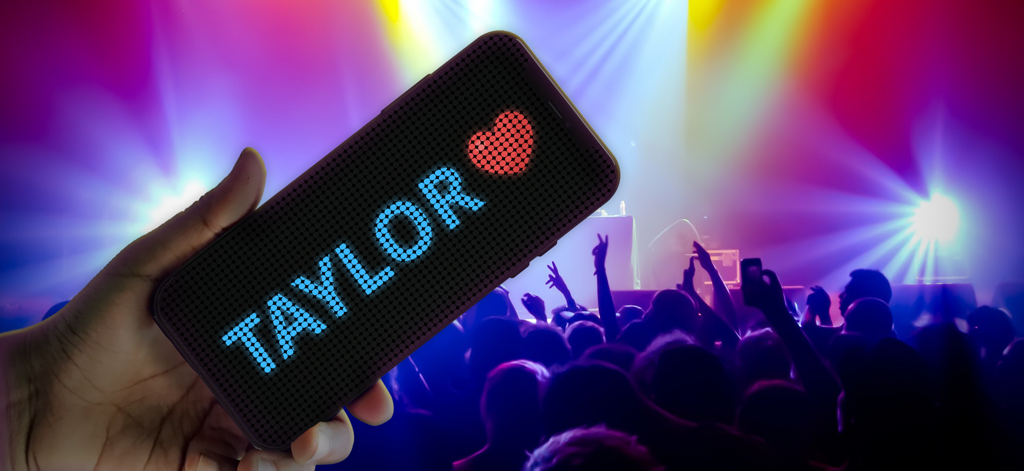 LED Banner: LED Scroller Board - Smartphone mostrando un cartel digital LED desplazable con el nombre Taylor y un corazón en un concierto en vivo
