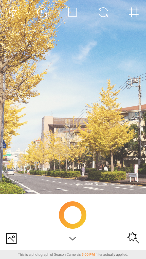 Une interface d'application de caméra montrant un filtre d'automne chaud appliqué à une photo d'arbres jaunes le long d'une rue.