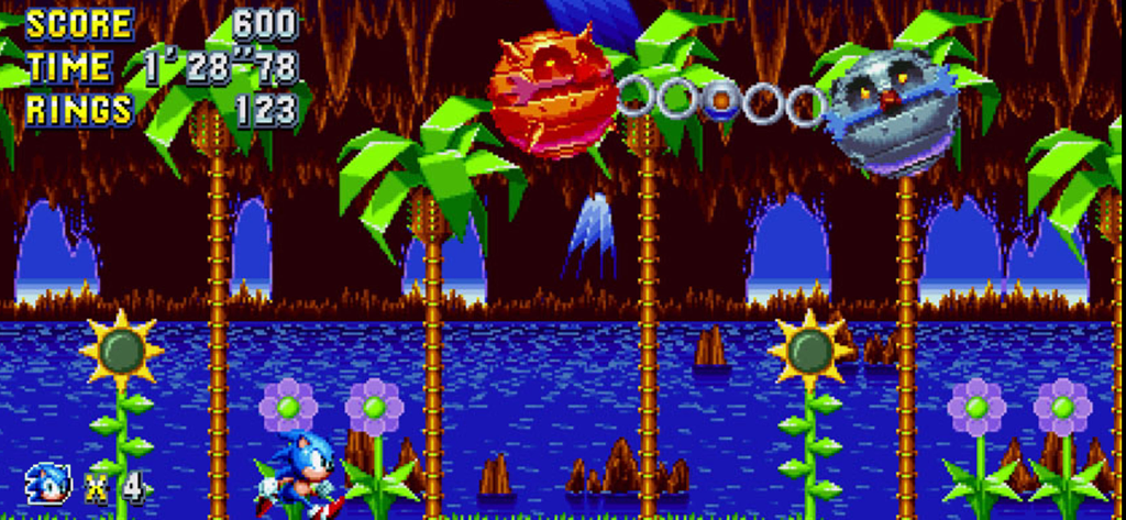 Sonic Mania Plus - NETFLIX - Sonic the Hedgehog corre attraverso un livello tropicale retrò pixel art durante una battaglia contro un boss con un nemico robotico incatenato