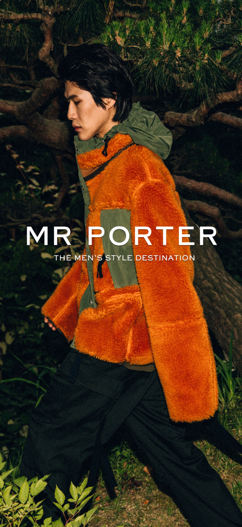 Un homme portant une veste polaire de luxe orange vif et un pantalon cargo foncé dans un décor forestier pour MR PORTER.