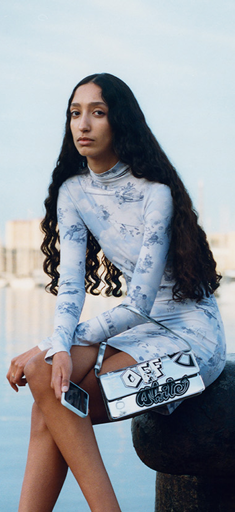 Off-White - A model in an Off-White printed dress holding a silver crossbody bag