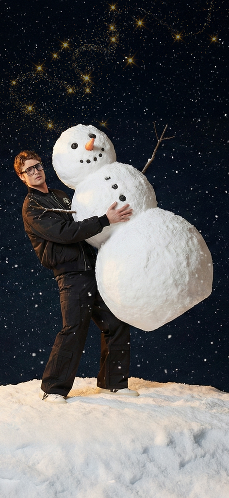 FashFed – Online Alışveriş - Ein Mann in einer stilvollen schwarzen Winterjacke und Cargohose umarmt einen großen Schneemann unter einem sternenklaren Nachthimmel