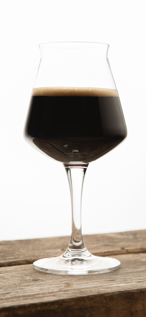 Craft Beer & Brewing Magazine - 러스트한 나무 테이블 위에 있는 줄기 달린 잔에 크리미한 베이지색 거품 머리가 있는 어두운 크래프트 맥주.