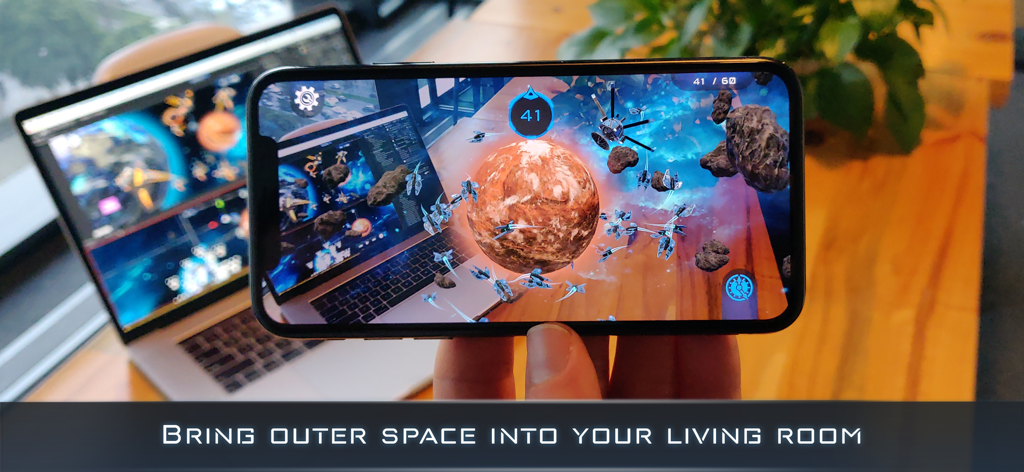 Una persona jugando al juego de estrategia espacial de realidad aumentada Cosmic Frontline AR en un iPhone mostrando naves espaciales y planetas sobre un escritorio y un portátil