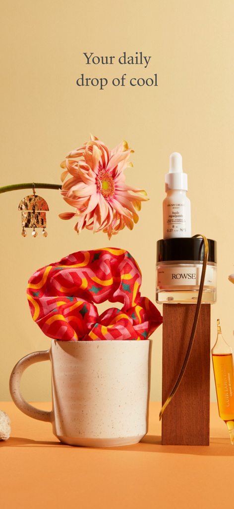 An aesthetic still life arrangement featuring curated skincare, jewelry, and a mug with the text Your daily drop of cool.