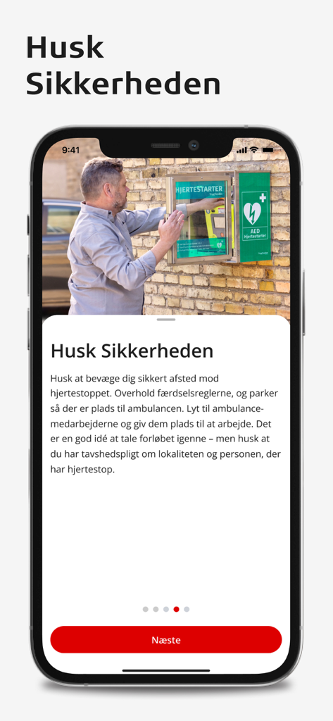 TrygFonden Hjerteløber - モバイルアプリ画面「安全を忘れないで」には、男性が壁のキャビネットからAEDを取り出している様子と、デンマーク語の安全指示が表示されています