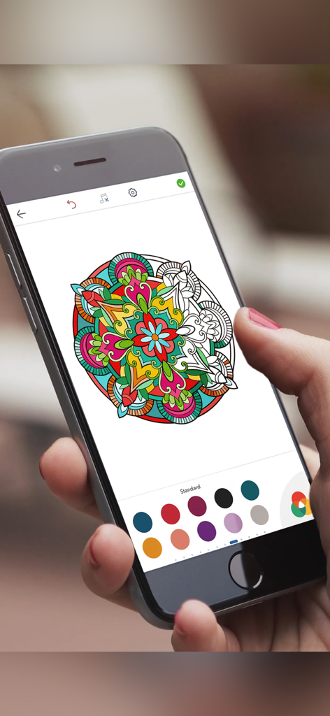 A woman coloring a detailed mandala on a smartphone app using a digital color palette.