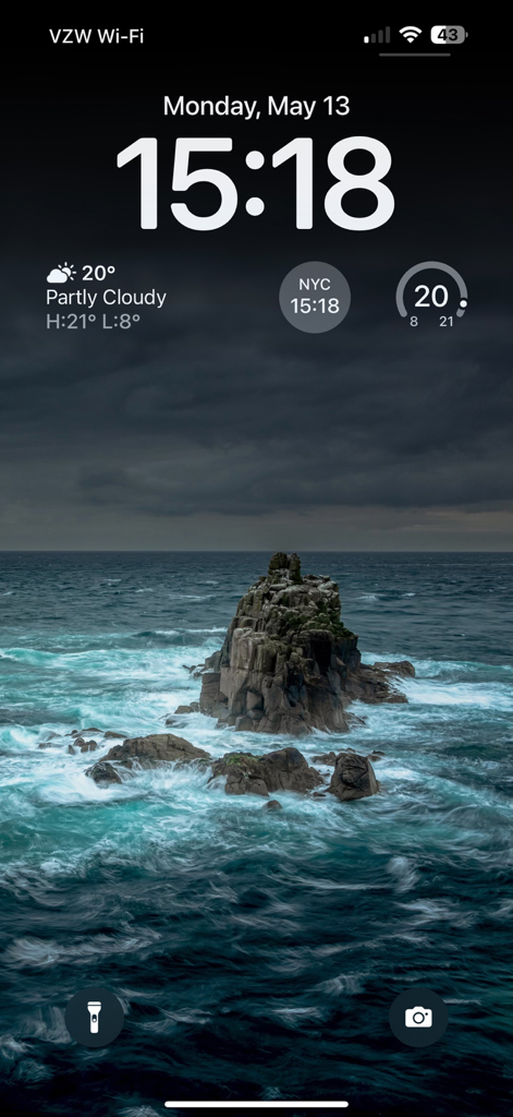 A 4K live wallpaper on an iPhone lock screen showing a dramatic rock formation in the crashing sea under a dark sky
