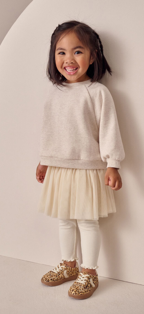 Next: Shop Fashion & Homeware - A smiling young girl wearing a beige sweatshirt and tutu skirt from the Next shopping app
