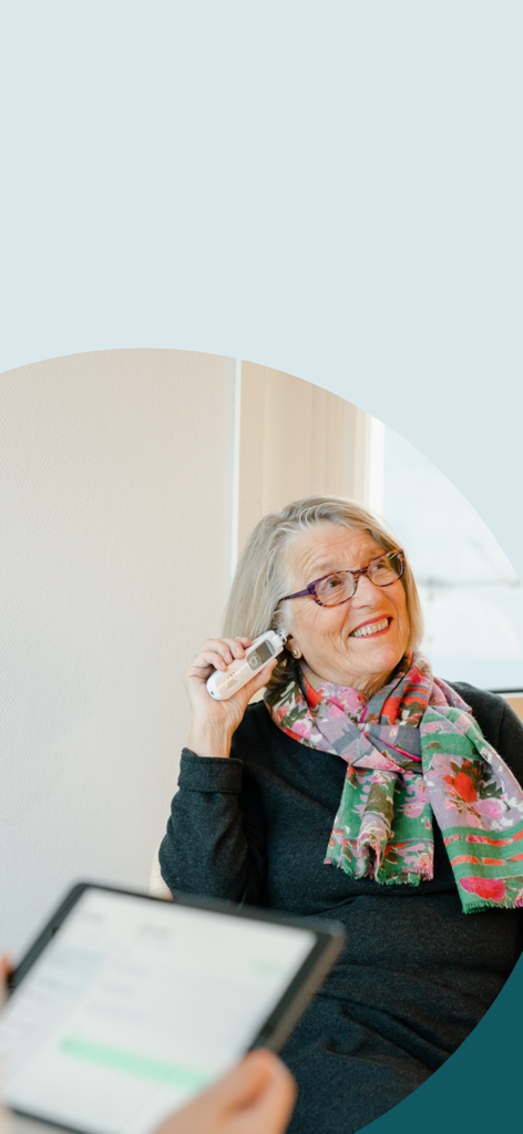 Dignio Prevent Go - An elderly woman uses a digital ear thermometer while a clinician monitors the data on a tablet