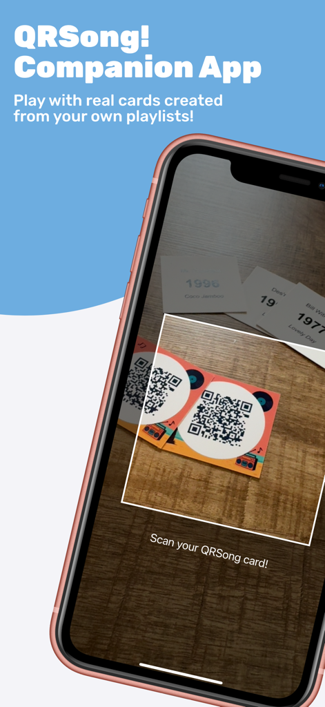 QRSong! - Pantalla de iPhone que muestra la interfaz de la aplicación complementaria QRSong escaneando una carta de música física con código QR sobre una mesa de madera