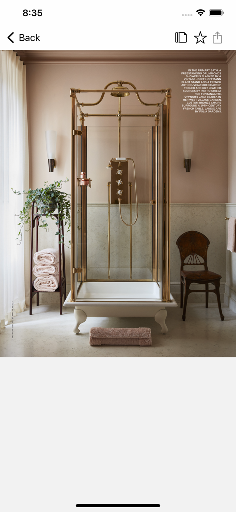Architectural Digest - A luxury bathroom interior featuring a brass-framed freestanding shower and vintage furniture as seen in the Architectural Digest app.