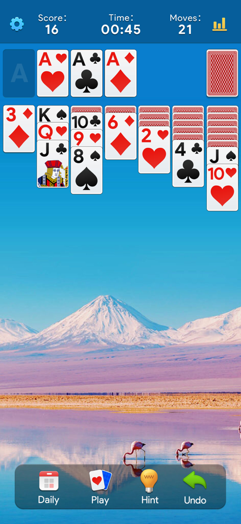 Solitaire Daily: Card Game - Pantalla del juego de cartas Solitario Diario mostrando la jugabilidad clásica de Klondike sobre un relajante fondo de montañas y flamencos