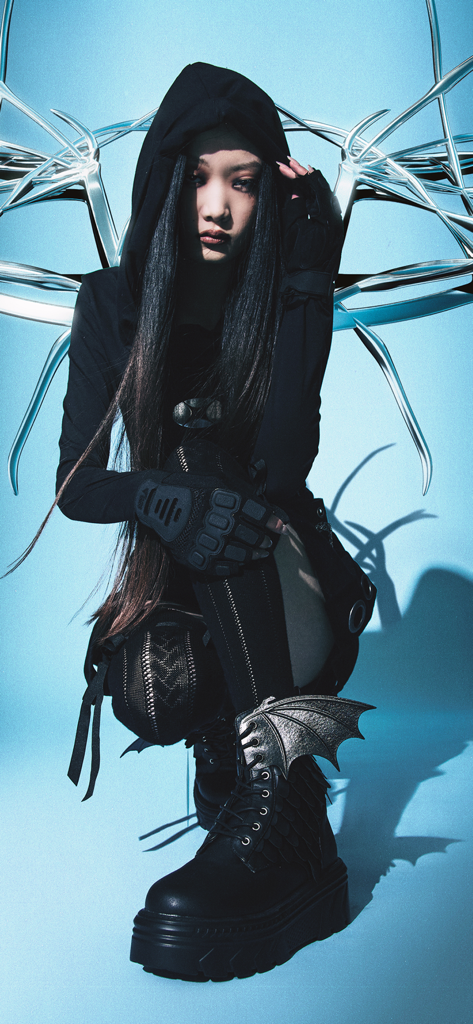 KOI Footwear. - Una modella indossa stivali con plateau neri Koi Footwear con dettagli ad ali di pipistrello argentate in uno stile moda goth alternativo.