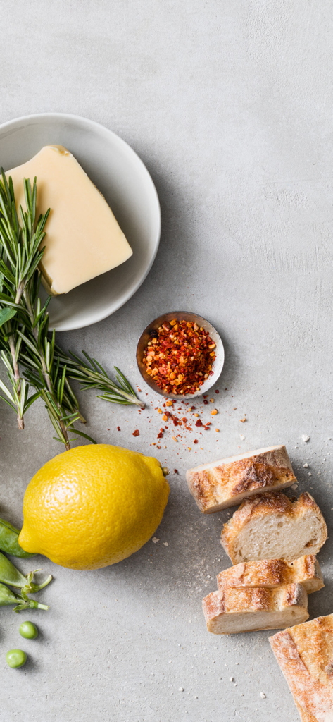 A top-down view of fresh ingredients including a lemon, sliced bread, rosemary, and spices