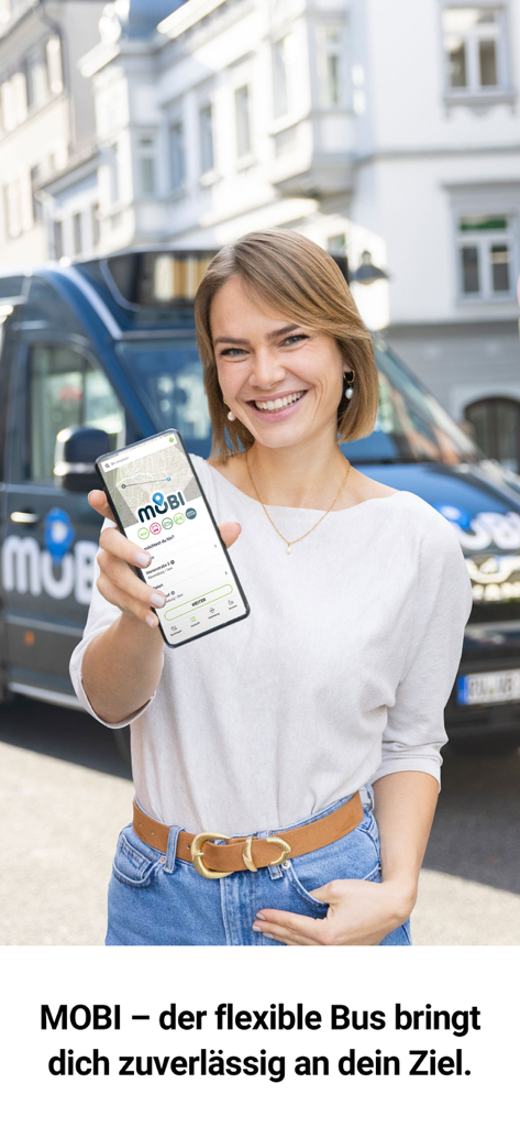 tws.mobil - 青いMOBIシャトルバスの前にtws.mobilアプリを表示したスマートフォンを持つ若い女性。