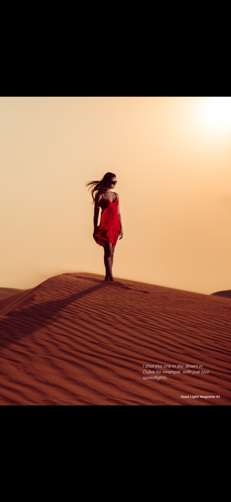 Ritratto editoriale di una donna in abito rosso su una duna di sabbia con illuminazione speedlight