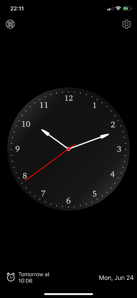 Una esfera de reloj analógica minimalista sobre un fondo negro con una esfera gris oscuro y una visualización de alarma próxima.