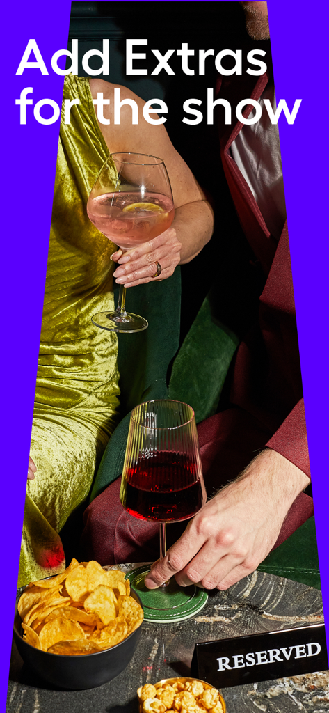 Zwei Personen in eleganter Kleidung genießen Cocktails und Snacks an einem reservierten Theatertisch in der Lounge.