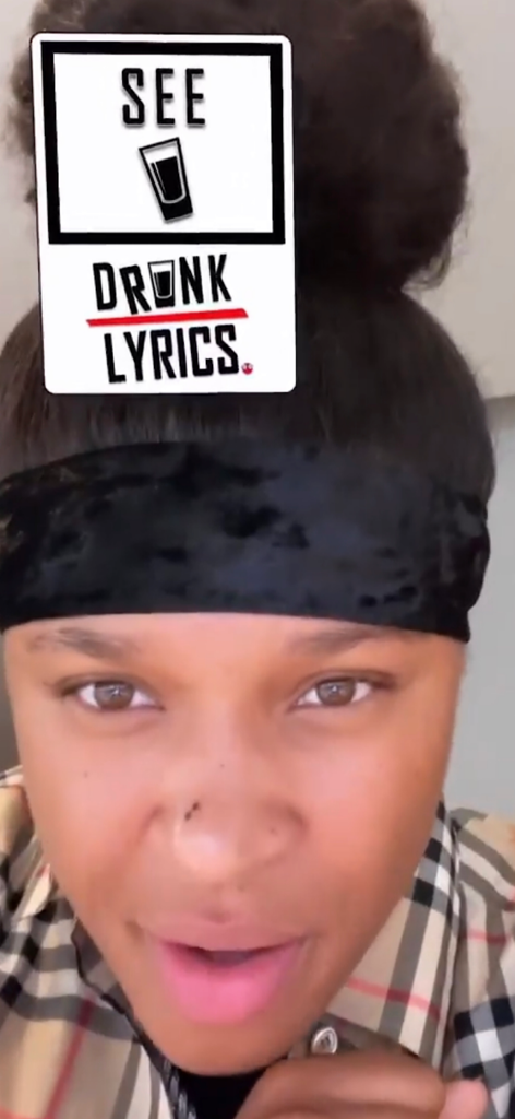 A woman playing the Drunk Lyrics party game with a digital card displaying the word see on her forehead.