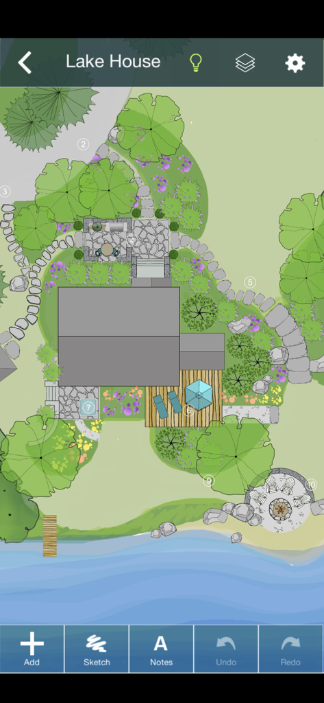 Vue de dessus d'une conception paysagère 2D pour une maison au bord du lac montrant des arbres, des chemins en pierre, une terrasse et un foyer