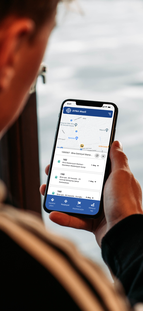 AYNA MaaS - Una persona sosteniendo un smartphone que muestra los tiempos de llegada de autobuses en tiempo real y un mapa de tránsito en la aplicación AYNA MaaS.