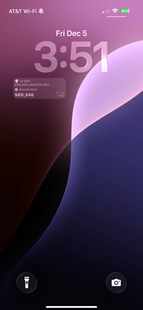 Tela bloqueada do iPhone com um widget exibindo dados de dívida nacional dos EUA e preço do Bitcoin