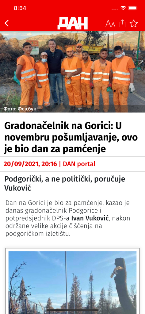 A news article on the DAN portal mobile app featuring a headline and a photo of a group of workers with a public official.