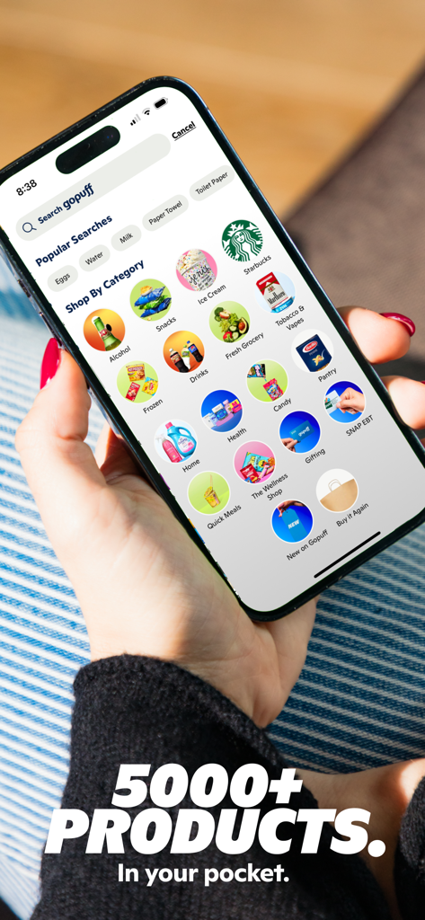 Gopuff - Food & Drink Delivery - A hand holding a smartphone displaying the Gopuff app Shop By Category screen with various products like snacks alcohol and groceries