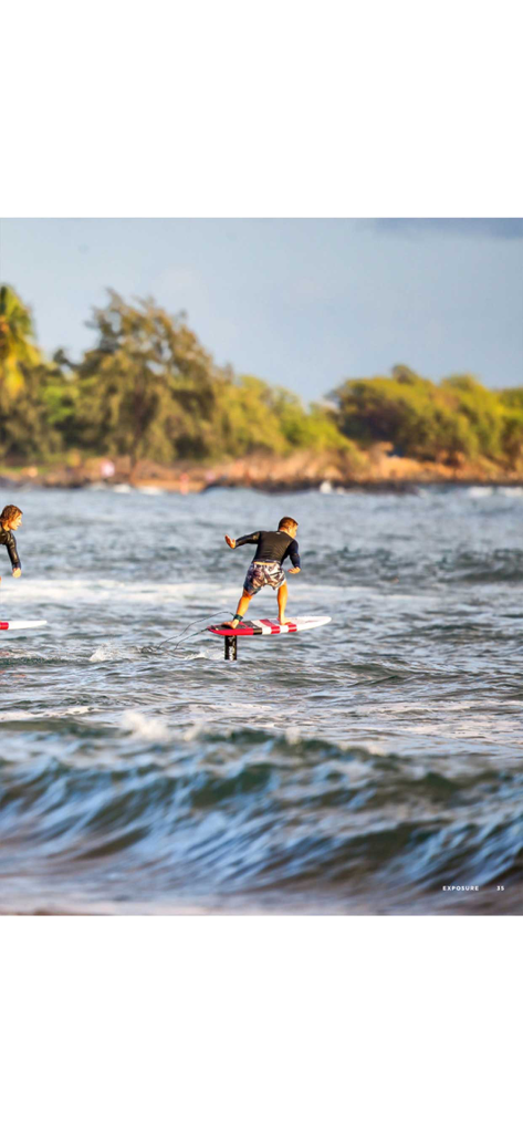 Foiling Magazine - Ein Surfer auf einem Hydrofoil-Board über dem Wasser an einer tropischen Küste