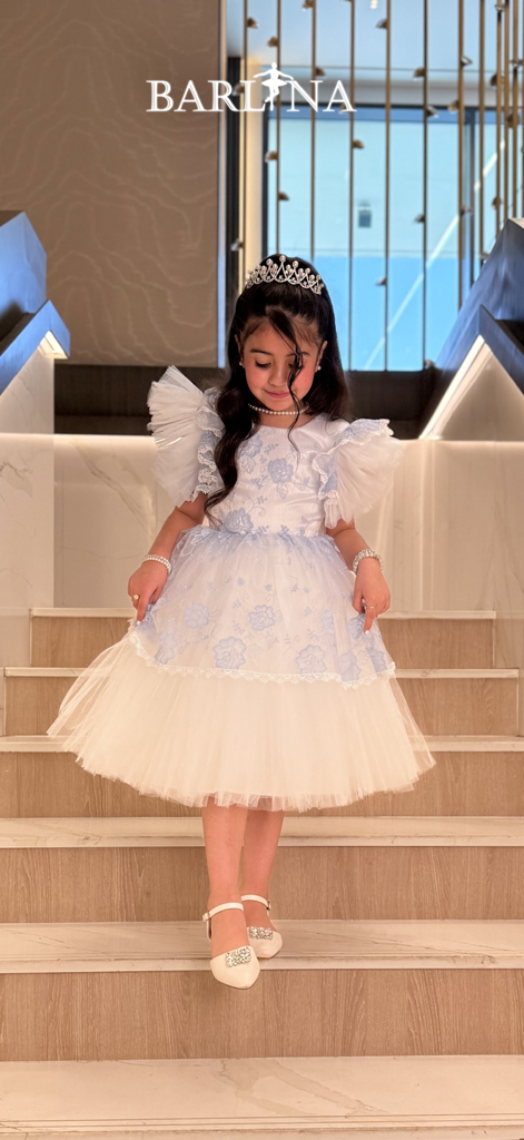 A young girl wearing a white and blue luxury modest dress with a tiara from Barlina