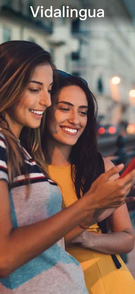 Zwei lächelnde Frauen, die die Vidalingua Italienisch-Lern-App auf einem Smartphone in einer städtischen Umgebung benutzen