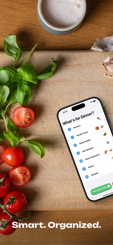 What's for dinner planner - Smartphone showing a meal planning list with food emojis on a wooden board with fresh tomatoes and basil
