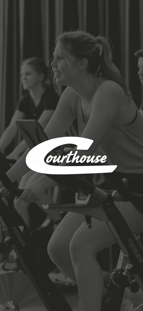 Courthouse Clubs - A woman smiling while riding a stationary bike in a fitness class at Courthouse Health and Fitness.