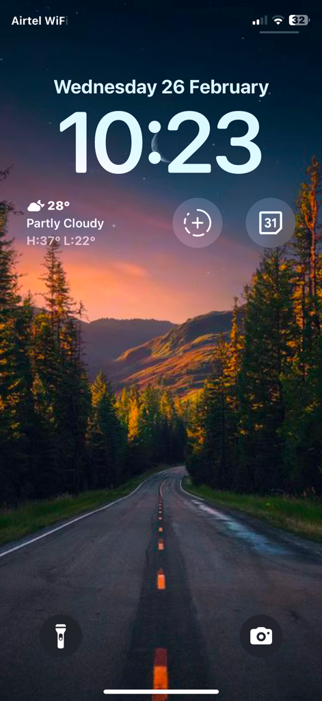 Wallpics - Live Wallpaper,Zed - Pantalla de bloqueo del iPhone mostrando un fondo de pantalla de naturaleza escénica de una carretera sinuosa en un bosque al atardecer