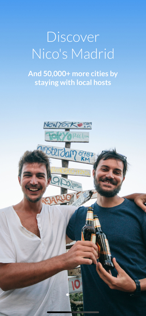 Couchsurfing Travel App - Dois jovens viajantes sorrindo com bebidas em frente a um poste de sinalização da cidade