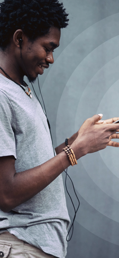 Un hombre joven sonriendo mientras usa un smartphone y auriculares para escuchar música con la aplicación Volume Bass Booster