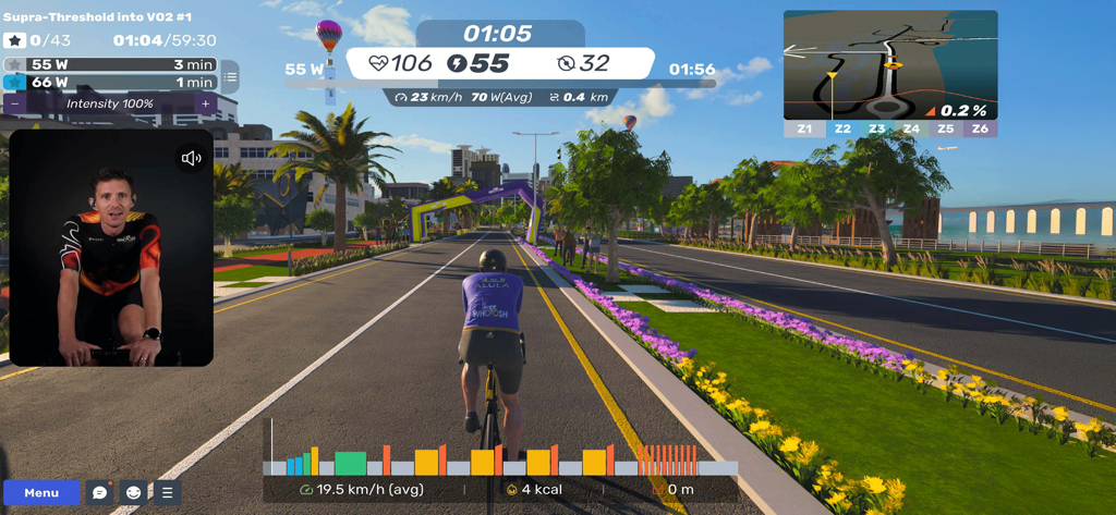 MyWhoosh virtual cycling interface showing a rider in a simulated environment with a coach video and performance metrics