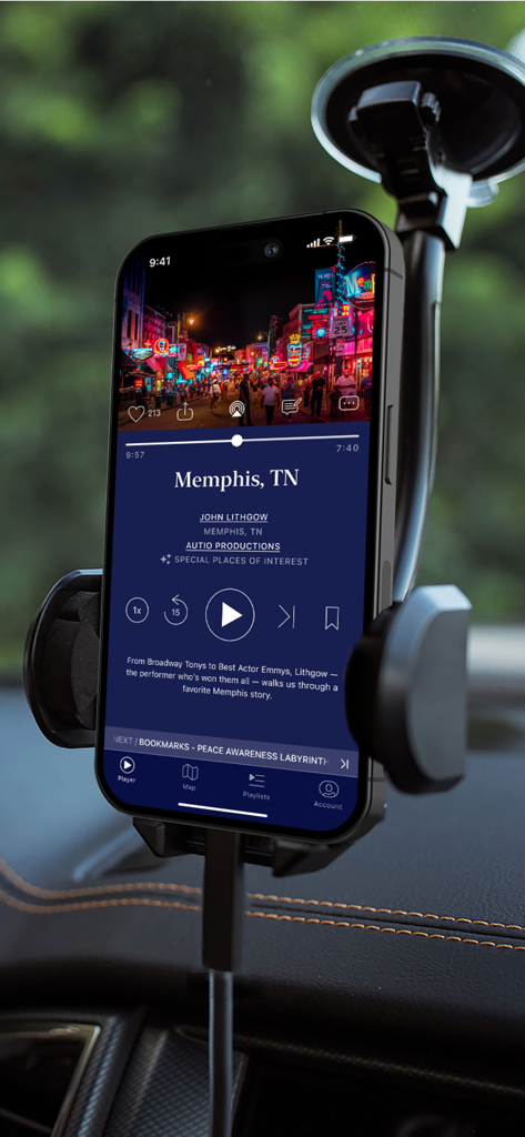 Autio: Road Trip & Travel App - iPhone in a car mount showing the Autio app audio player with a story about Memphis Tennessee narrated by John Lithgow